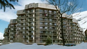 Monikerroksinen hotelli, jossa on parvekkeet, lumipeitteinen maa ja taustalla kohoavat vuoret.