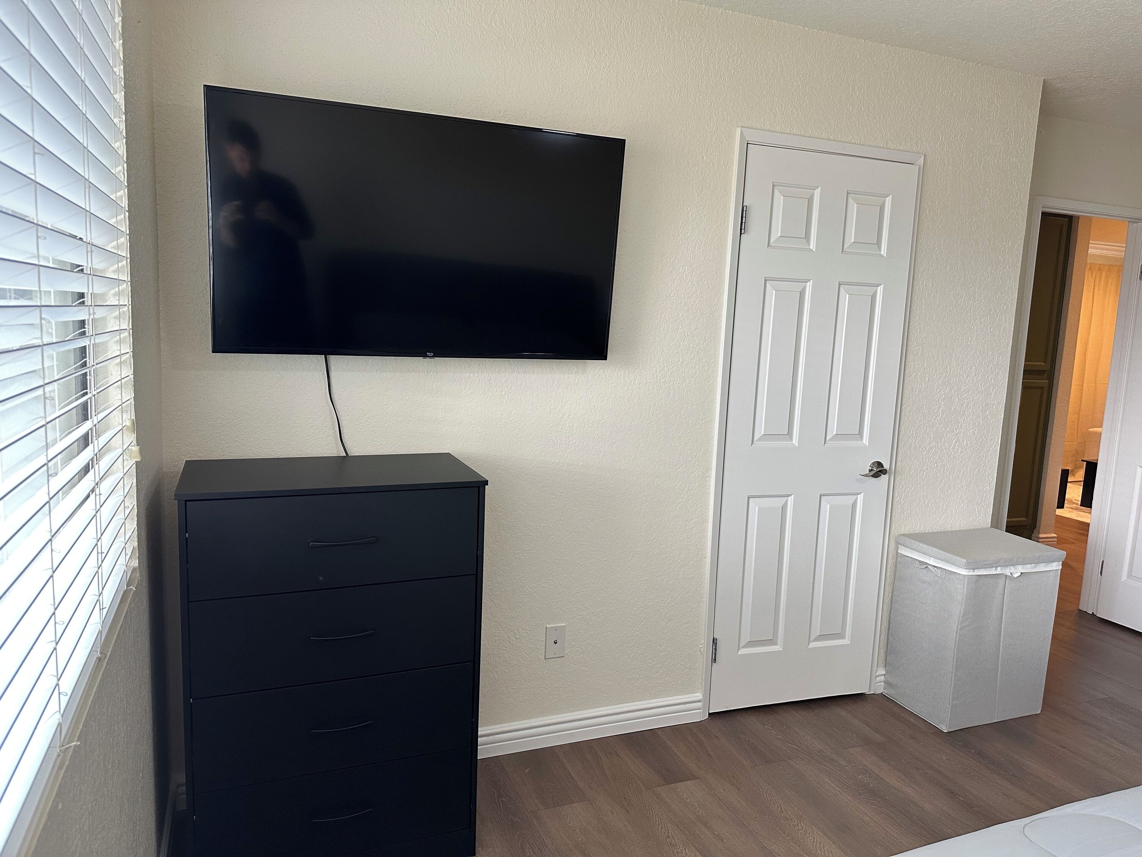 A room with a flat-screen TV mounted on the wall, a dark-colored cabinet, a white door, and a small white object on the floor.