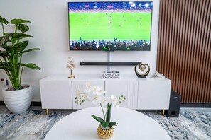 Un salon moderne avec un téléviseur à écran plat, un meuble de rangement blanc et une petite table blanche ornée d’une orchidée.
