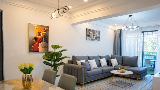 Una sala de estar moderna con un sofá gris, una mesa de comedor con sillas, una mesita de centro y un ventanal con cortinas.