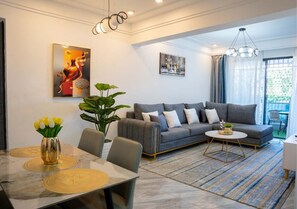 Un salon moderne avec un canapé gris, une table à manger avec des chaises, une table basse et une grande fenêtre avec des rideaux.