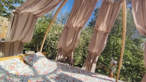 Ein Bett mit floraler Bettwäsche, ein rundes Oberlicht und Vorhänge in einem Zimmer mit Blick ins Grüne.