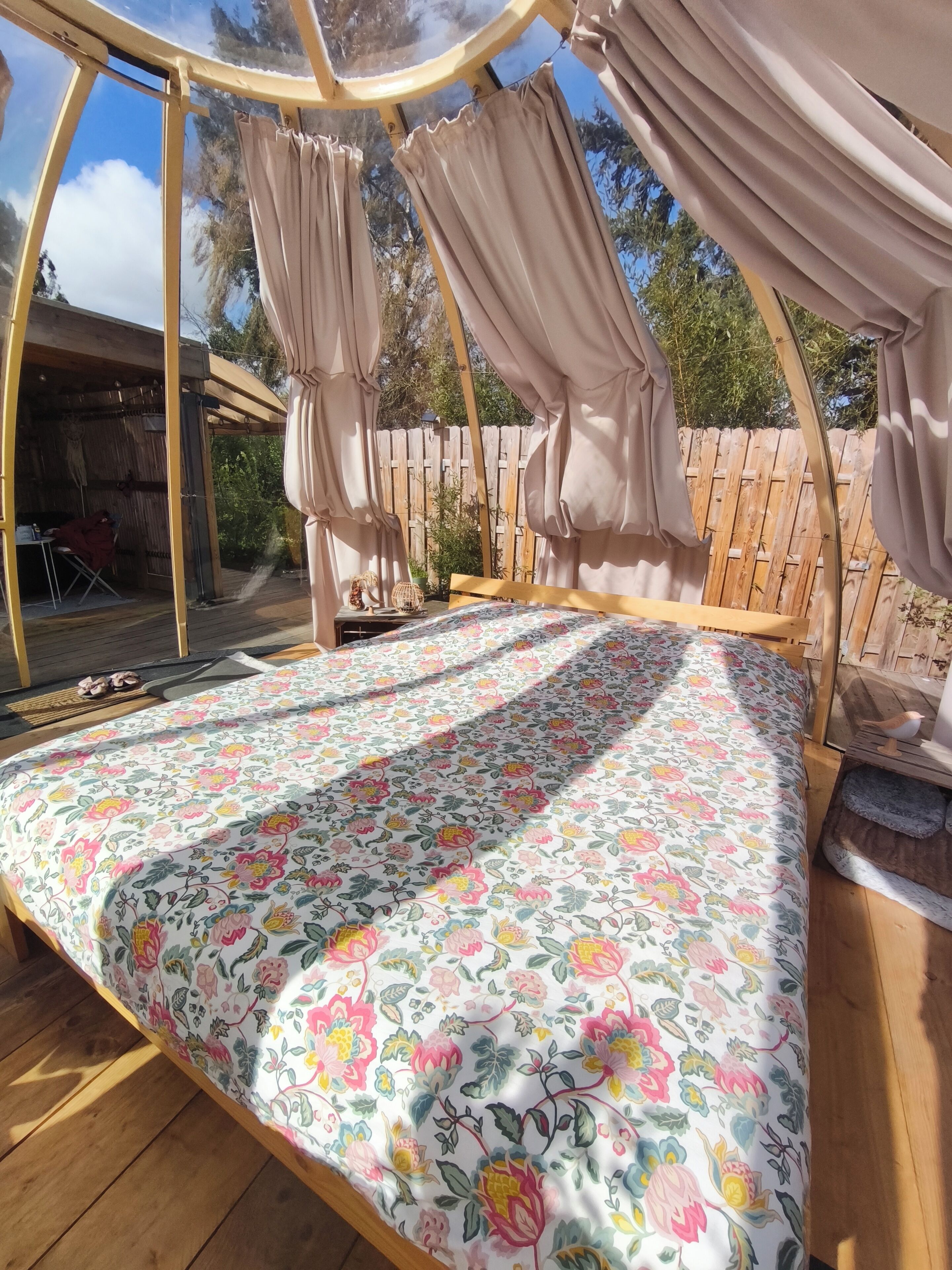 A cozy outdoor sleeping area with a canopy bed, a wooden deck, and a view of the surrounding garden.