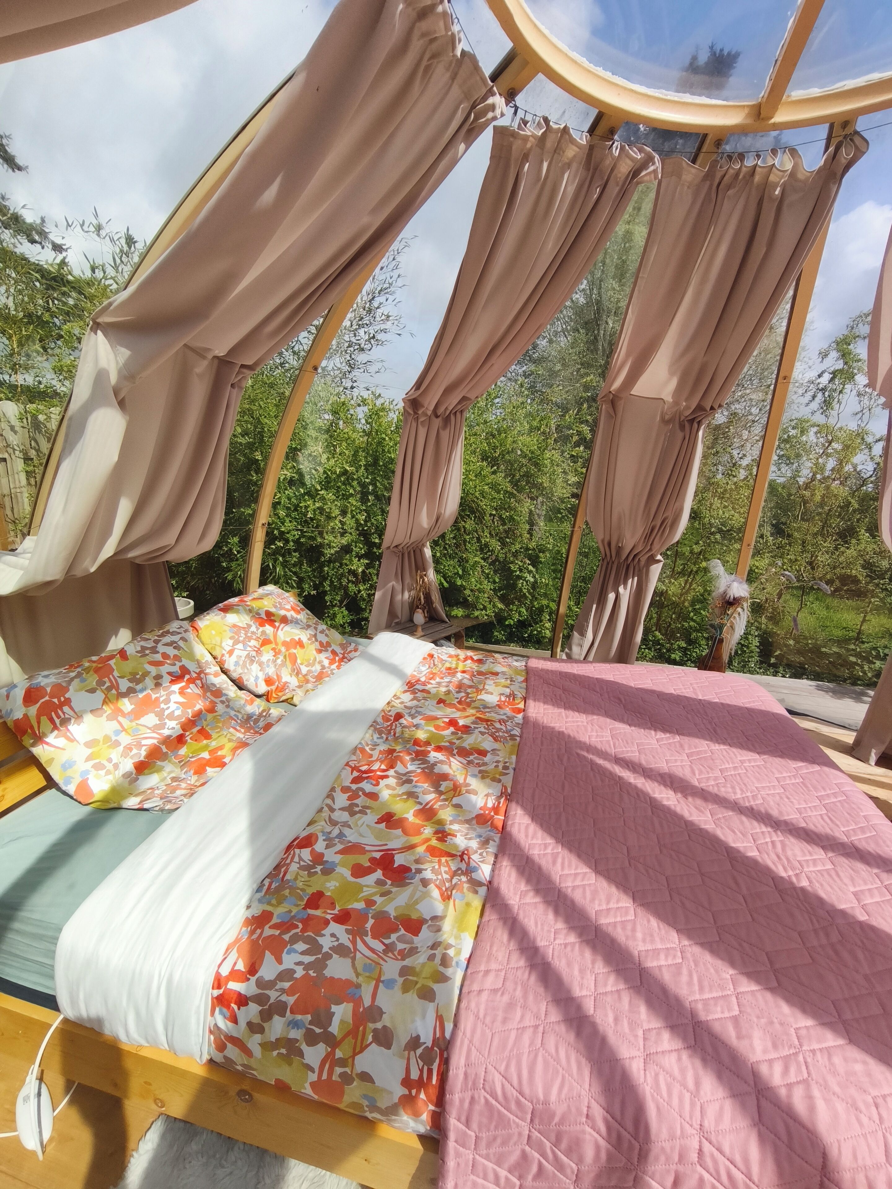 A tent-style room with a bed, curtains, and a view of greenery.