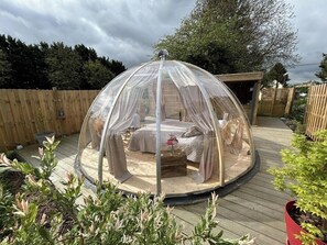 A round, transparent gazebo with a bed and a small table, surrounded by a wooden deck and potted plants. - O'fun'enbulle Unusual dome with private spa in a natural, relaxing setting (Mazinghien)