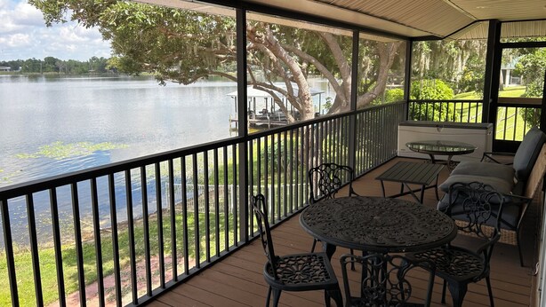 A covered outdoor area with a view of a lake, a table with chairs, and a small seating area. - Cozy Snowbird Retreat on Beautiful Lake June. Monthly Winter Rates (Lake Placid)