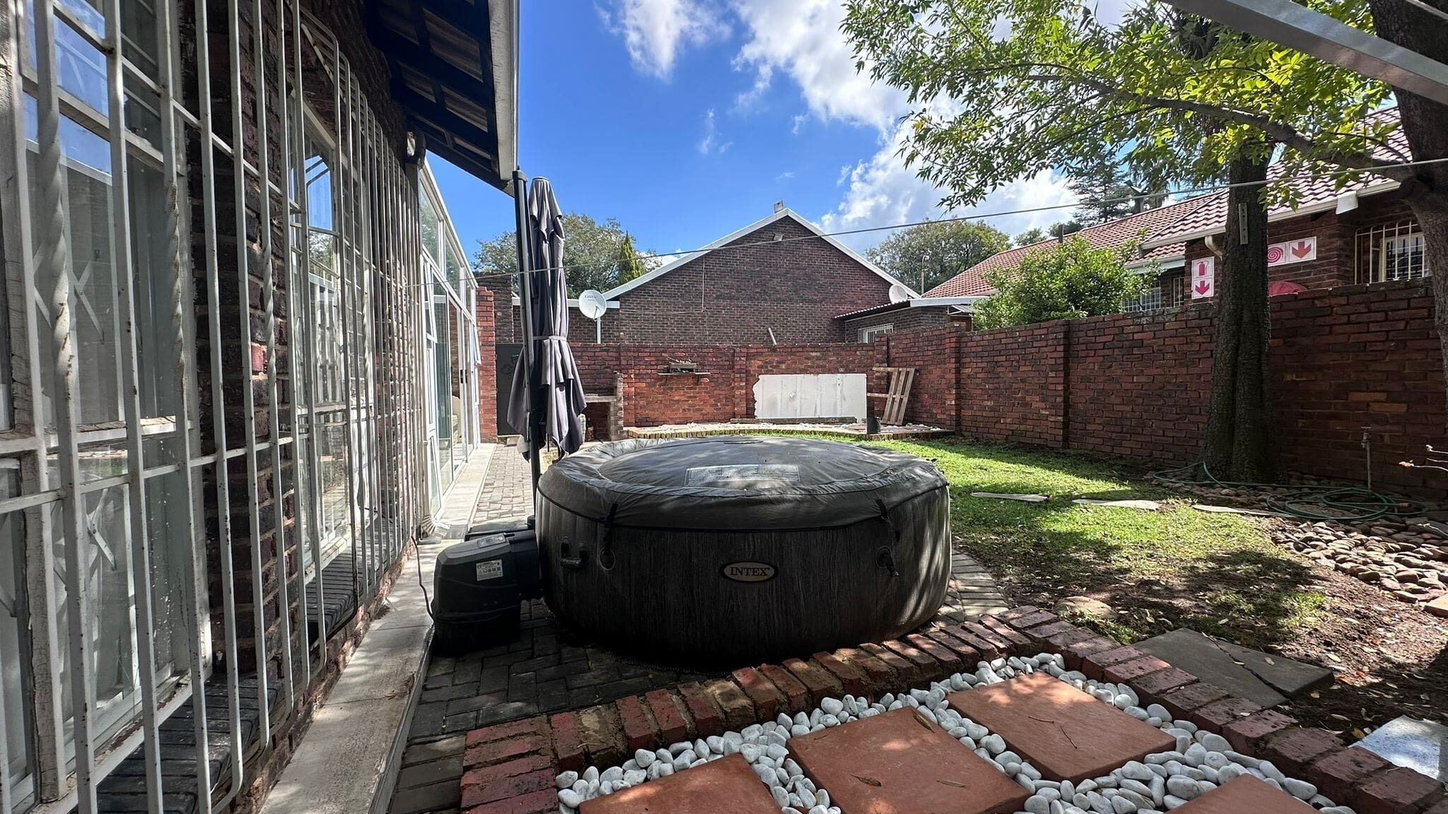 Un jardín trasero con un jacuzzi, un muro de ladrillo y una casa con antena parabólica.