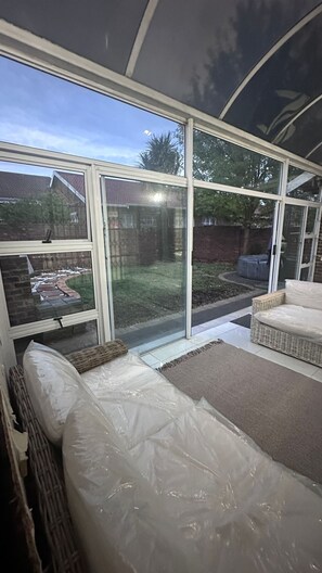 A sunroom with large windows, a wicker sofa, and a covered patio area.