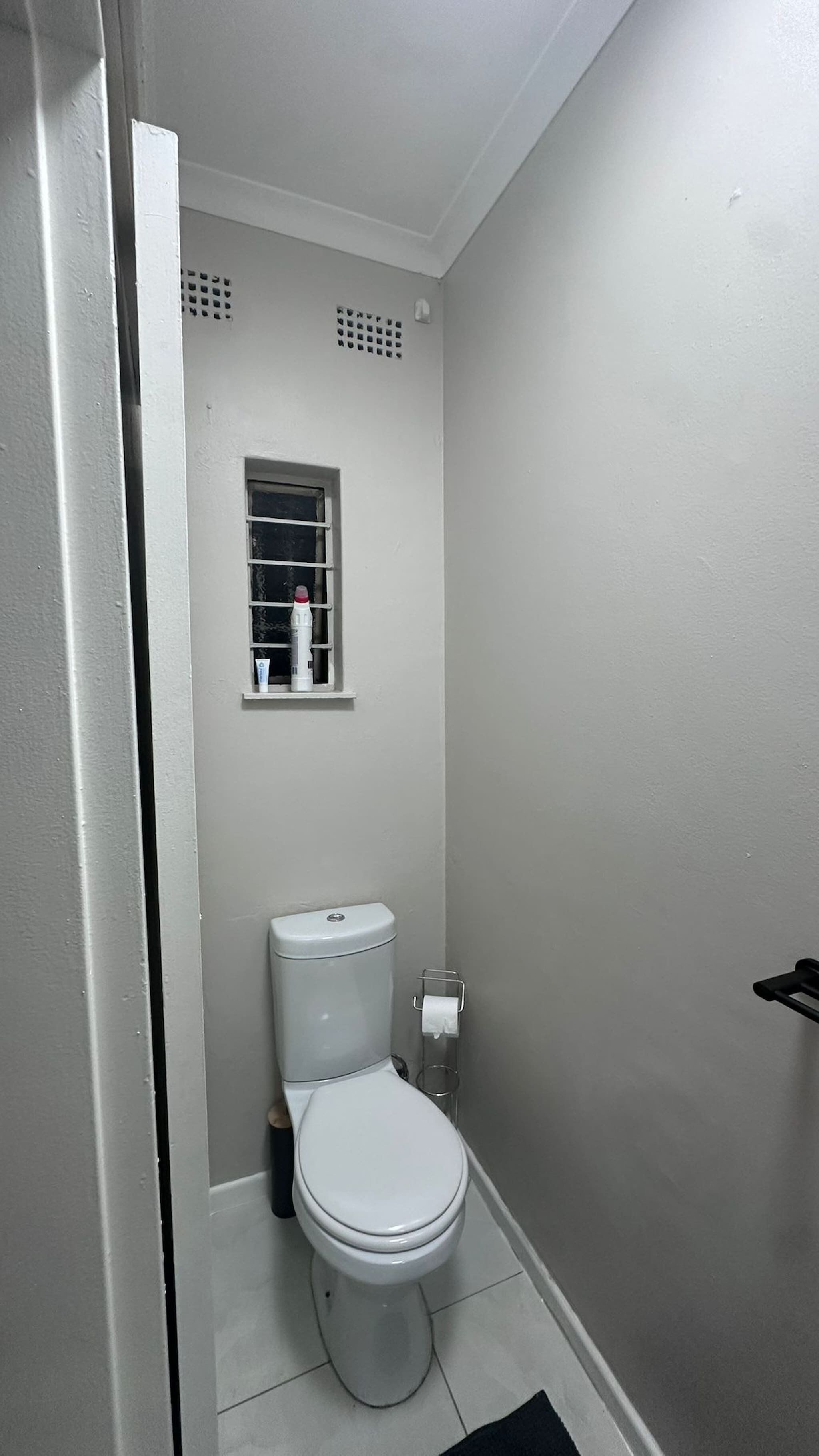Un baño pequeño y blanco con inodoro, ventana y perchero.