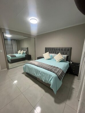 Un dormitorio con una cama grande, una mesita de noche, un espejo y una lámpara en el techo.