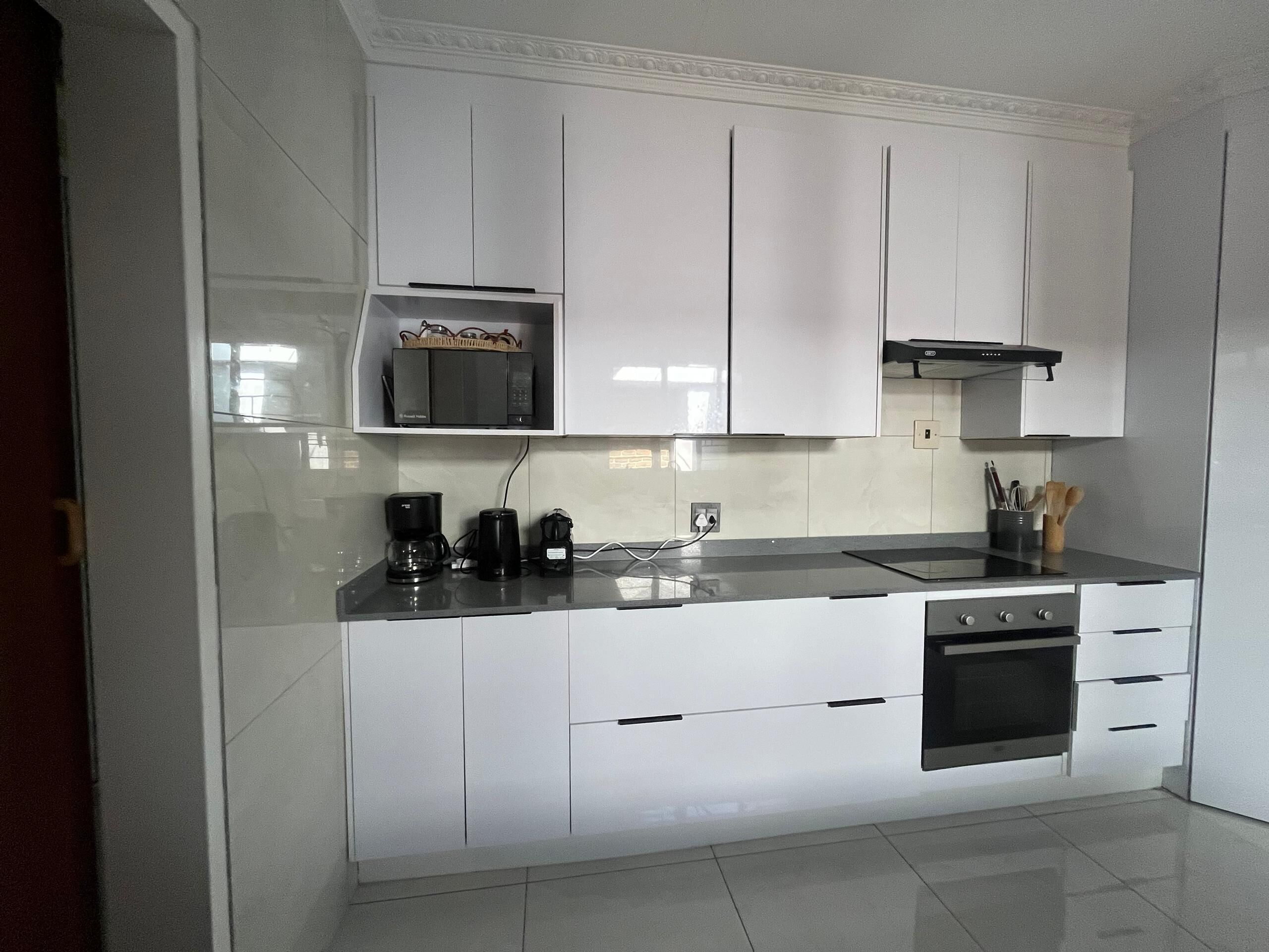 A modern kitchen with white cabinets, a black countertop, a coffee maker, and an oven.