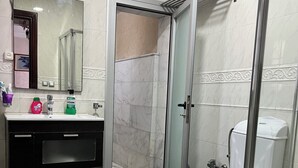 Et moderne badeværelse med en glasbrusekabine, et hvidt toilet, en sort kommode med et spejl og en vask.
