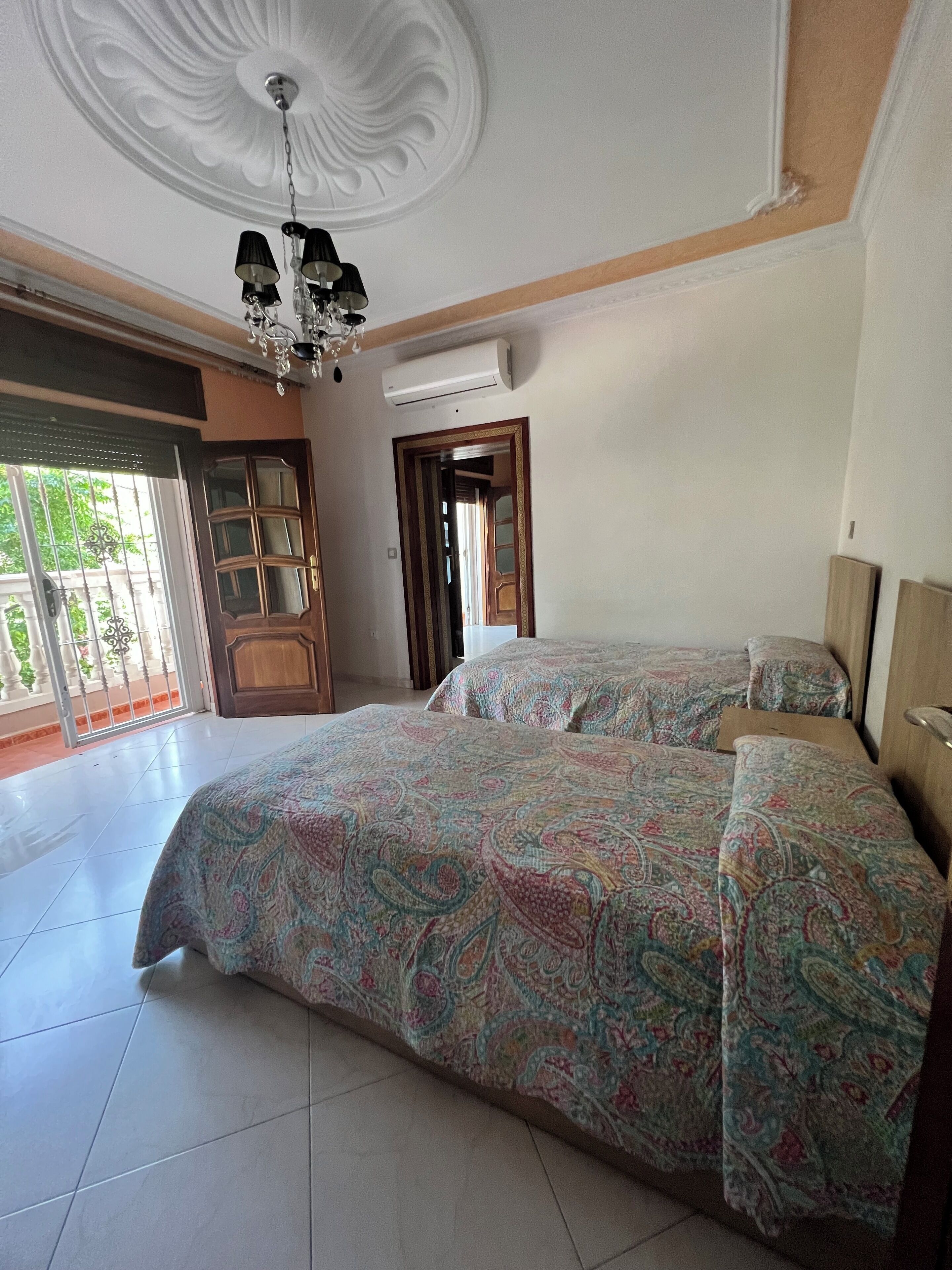 Une chambre avec deux lits, un lustre, un appareil de climatisation et une vue sur l’extérieur.