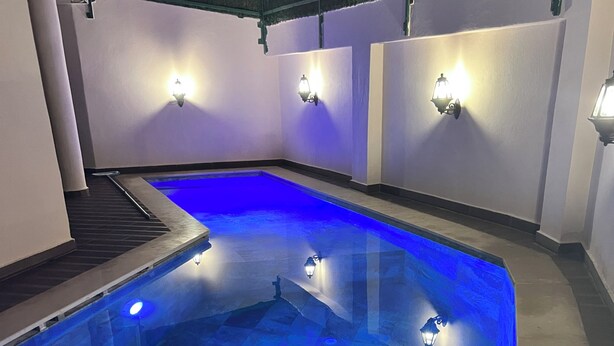En swimmingpool med blå belysning, omgivet af vægge med lysarmaturer.