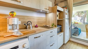 A modern kitchen with wooden cabinets, a coffee maker, a kettle, and a window to the outside. - Cosy T2 Apartment Facing the Sea with Private Terrace, Tennis Court, and Beach Access (Sète)