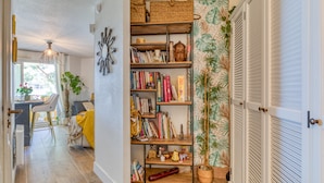 A room with a bookshelf, a dining area, and a door with louvered shutters. - Cosy T2 Apartment Facing the Sea with Private Terrace, Tennis Court, and Beach Access (Sète)