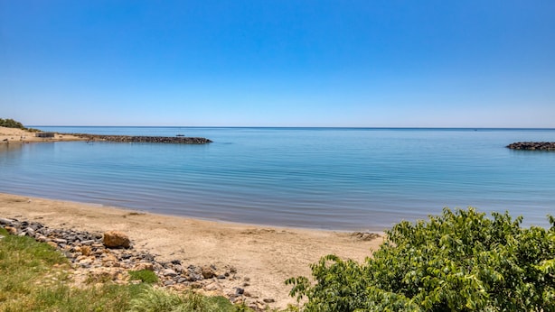 A beach with calm water, a rocky shoreline, and greenery in the foreground. - Cosy T2 Apartment Facing the Sea with Private Terrace, Tennis Court, and Beach Access (Sète)