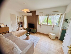Sala de estar com sofá, televisão, piso de madeira e janela com cortinas.