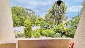 En balkon med et blåt bord og stole, en hængende lampe og udsigt over et grønt landskab.