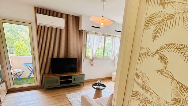 En moderne stue med et fladskærms-tv, trægulv, en sofa og et spiseområde med et bord og stole.