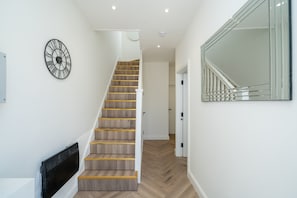 A staircase with wooden steps and a black handrail, a wall-mounted clock, and a large mirror. - Modern Attic Studio w/ Parking & Smart TV SW16 (London)