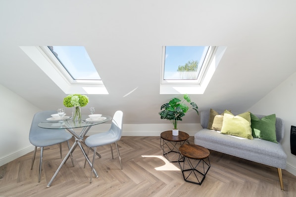 A modern loft with skylights, a dining area with a glass table, and a cozy seating area with a sofa. - Modern Attic Studio w/ Parking & Smart TV SW16 (London)