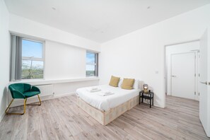 Ein Schlafzimmer mit Bett, Sessel, Nachttisch und großen Fenstern.