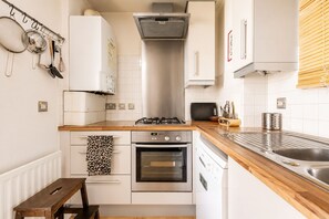 A compact kitchen with a gas stove, oven, and a wooden countertop. - Bright artistic flat in Central London (London)