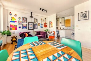 A modern living room with a wooden dining table, vibrant cushions, and a mix of wall art and decorative items. - Bright artistic flat in Central London (London)