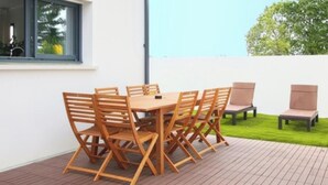 An outdoor patio with a wooden table and chairs, a small garden area, and a window with a view of trees. - New house Bretignolles sur Mer 1,5Km from the beach (Bretignolles-sur-Mer)