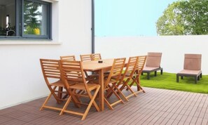 A patio with a wooden table and chairs, a window, and a view of a green lawn.