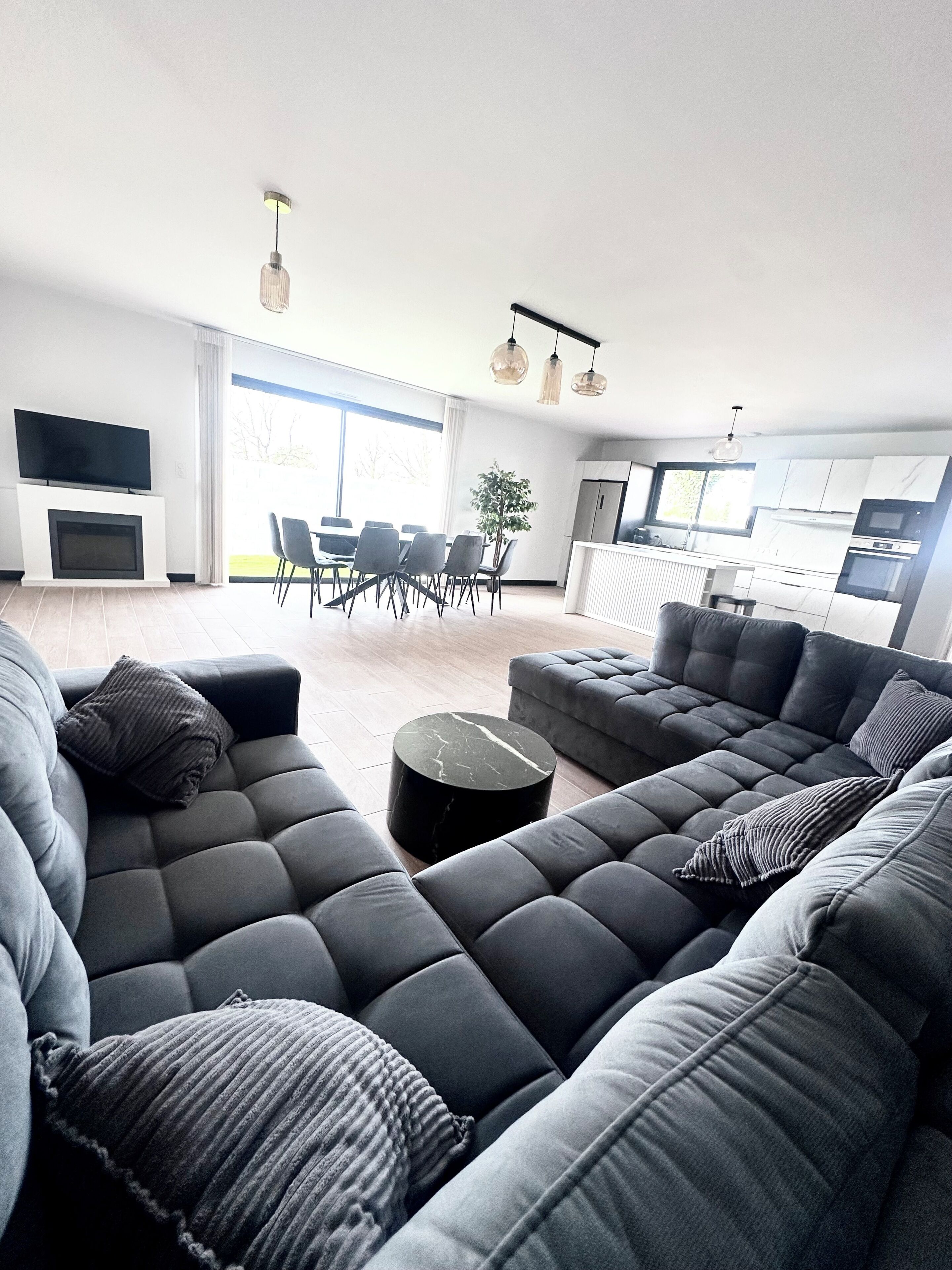 A modern living room with a sectional sofa, a dining area, and a kitchen.