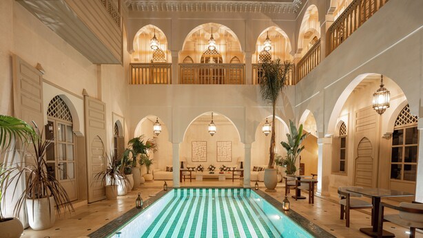 A pool with tiled walls and arches, surrounded by seating areas and potted plants. - Maison Zamane (Marrakech)