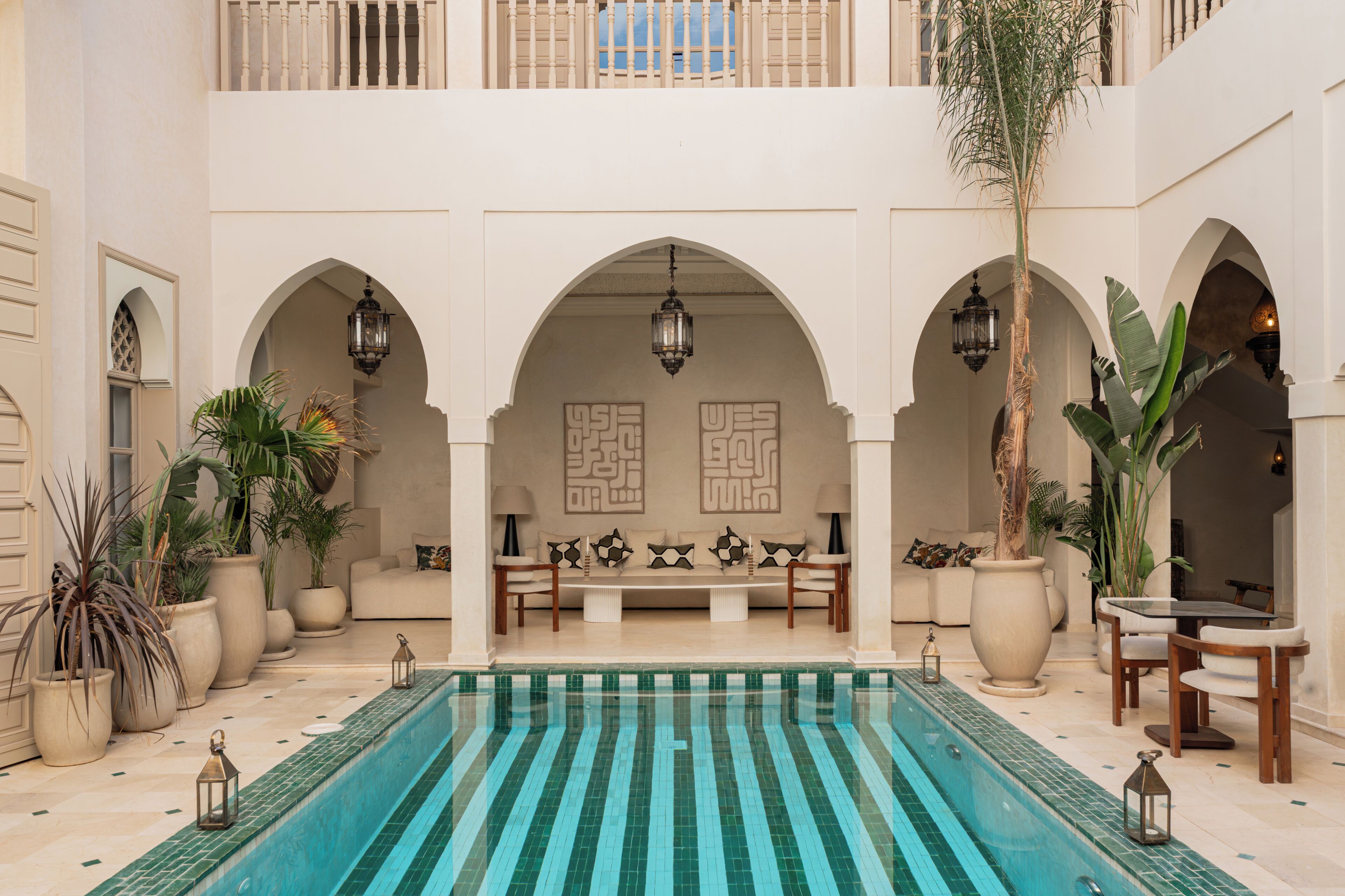 A pool area with a tiled floor, seating, and potted plants.