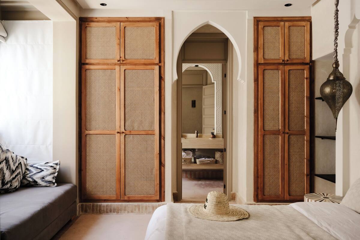 A bedroom with a bed, a sofa, a wardrobe with woven doors, a mirror, and a hanging lamp.