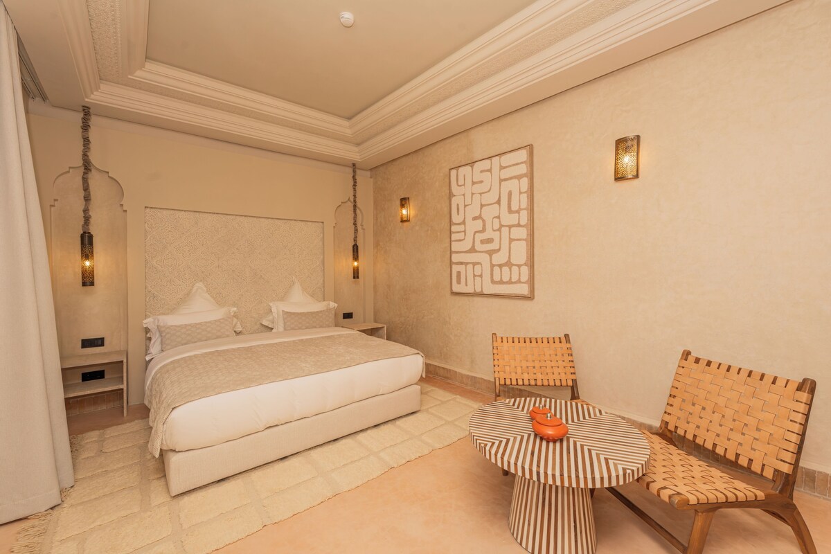 A bedroom with a bed, a small table with a chair, and decorative wall art.