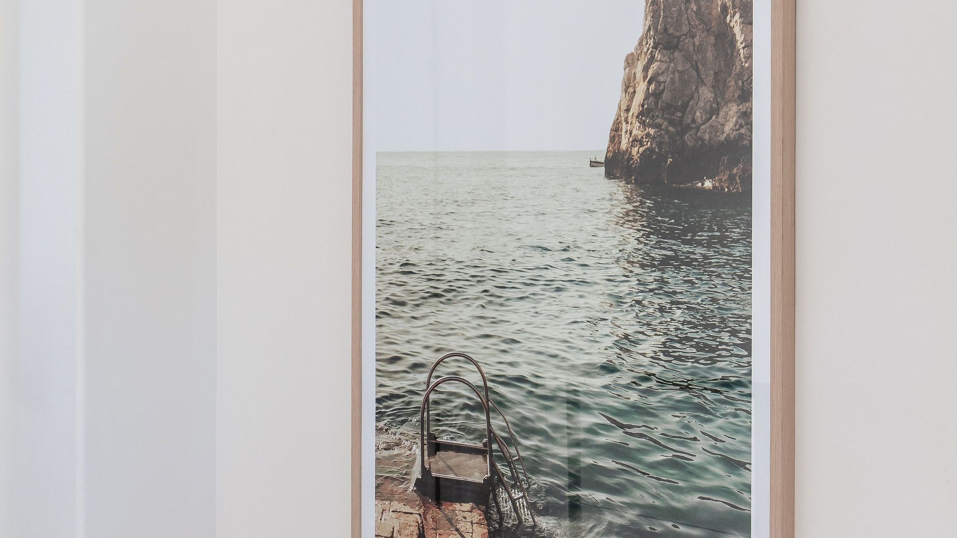 Fotografía enmarco de un litoral rocoso con aguas tranquilas y una escalera metálica que desciende hacia el mar.