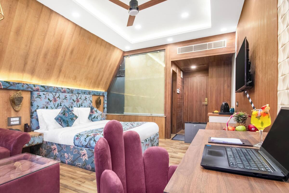 Una habitación de hotel moderna con una cama, un escritorio con una computadora portátil, una silla y un televisor.