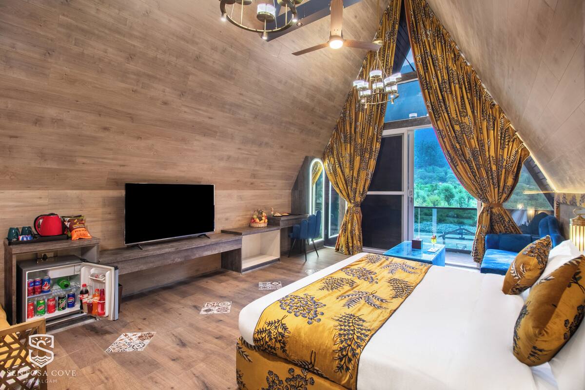 Un dormitorio con cama, televisor, refrigerador pequeño y balcón con vistas.