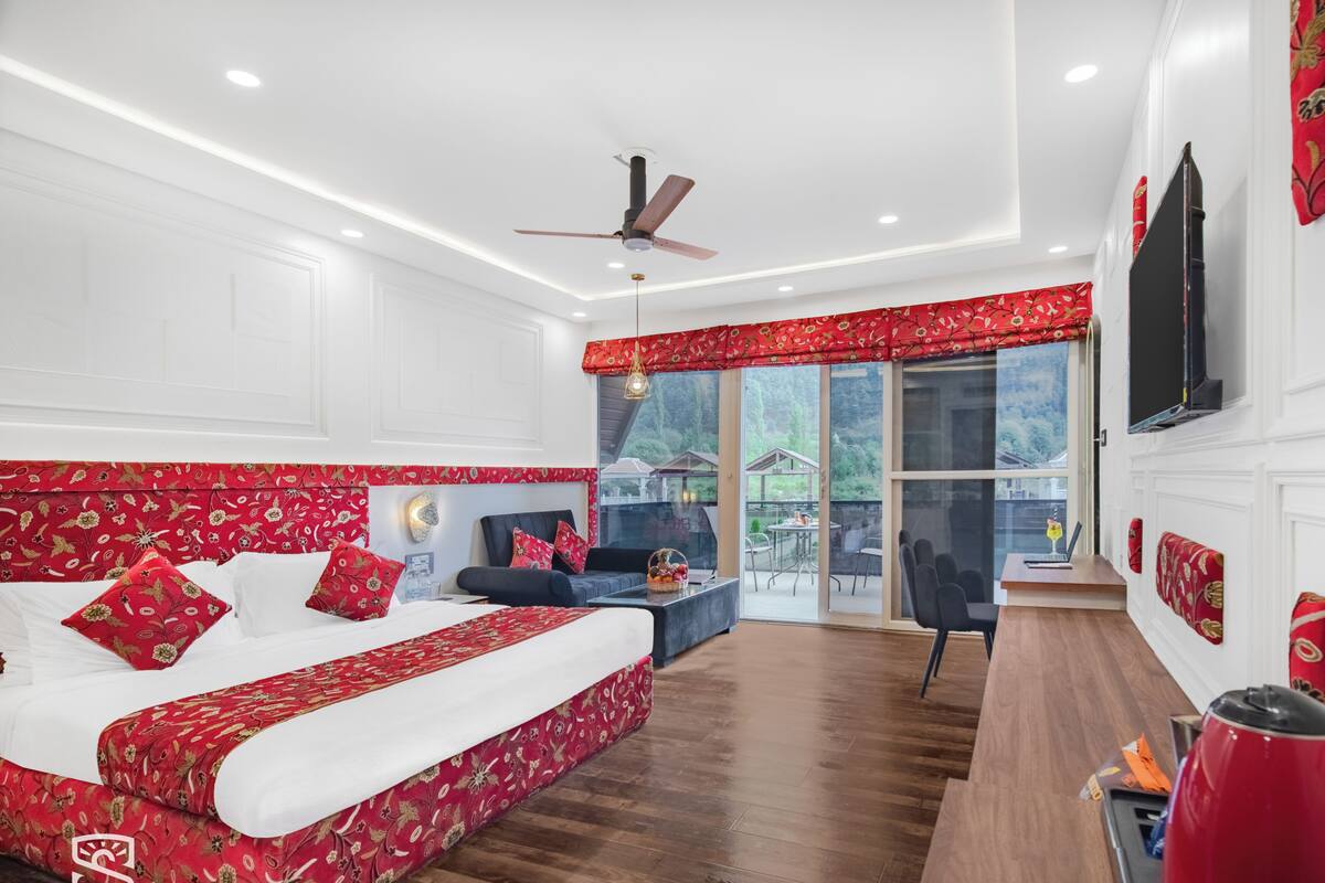 Un dormitorio con cama, escritorio, silla, ventilador de techo y ventana con vistas al exterior.