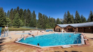A swimming pool with a wooden deck, a small building, and a forested hillside in the background. - Scenic Mountain Stay for Four (La Léchère)