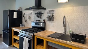 A kitchen with a black refrigerator, stove, and oven, wooden countertop, and a hanging light fixture.