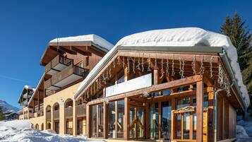 A wooden building with balconies and large windows, surrounded by snow.