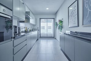 Eine moderne Küche mit Edelstahlgeräten, einer zentralen Kochinsel und Blick durch eine Glastür ins Freie.