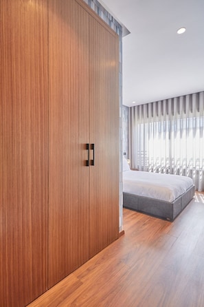 Ein Schlafzimmer mit großem Kleiderschrank, einem Bett und einem Fenster mit durchsichtigen Vorhängen.
