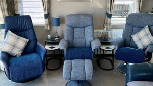 Ein Zimmer mit drei blauen Sesseln, einem zentralen Sofa und einem kleinen Tisch mit einer Lampe.