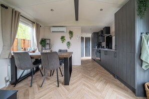 Eine moderne Küche mit Fischgrätparkett, grauen Schränken und einem Essbereich mit Holztisch und grauem Stuhl.