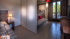 Ein Schlafzimmer mit Bett, Nachttisch, Lampe, Kleiderschrank, Sofa, einer roten Hängeleuchte, einem Fernseher und Blick ins Freie.