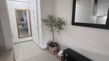 A hallway with a potted plant, a bench, a mirror, and a door leading to another room.