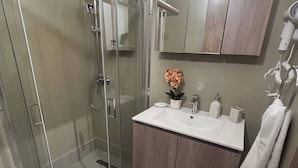 A modern bathroom with a glass shower enclosure, a vanity with a sink, and a mirror above the vanity. - Vasili's Mini Villa in Nafplio With Shaded Parking (Nafplio)